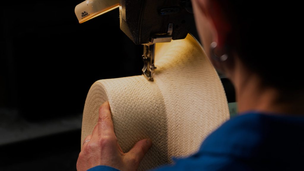 Artesana cosiendo el ala de un sombrero de paja a máquina.