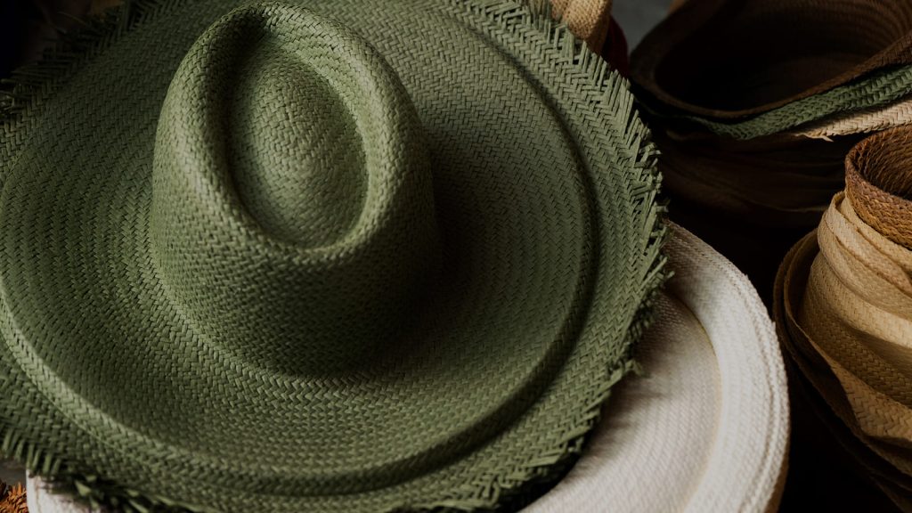 Sombrero panamá de paja verde tejido a mano junto a rollos de paja natural y otros sombreros.