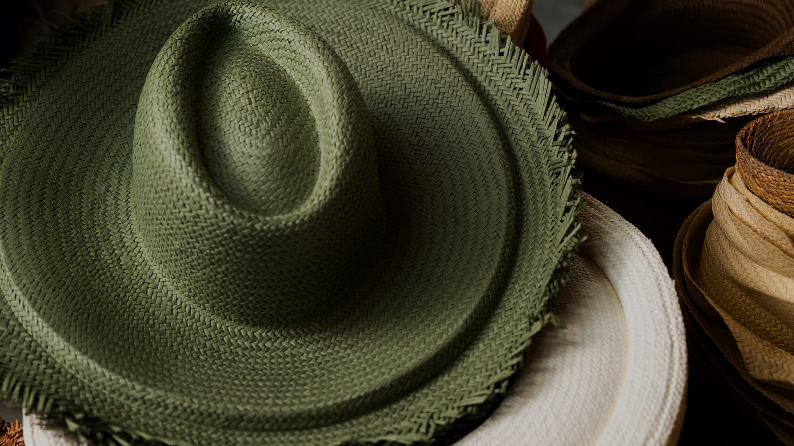 Sombrero panamá de paja verde tejido a mano junto a rollos de paja natural y otros sombreros.
